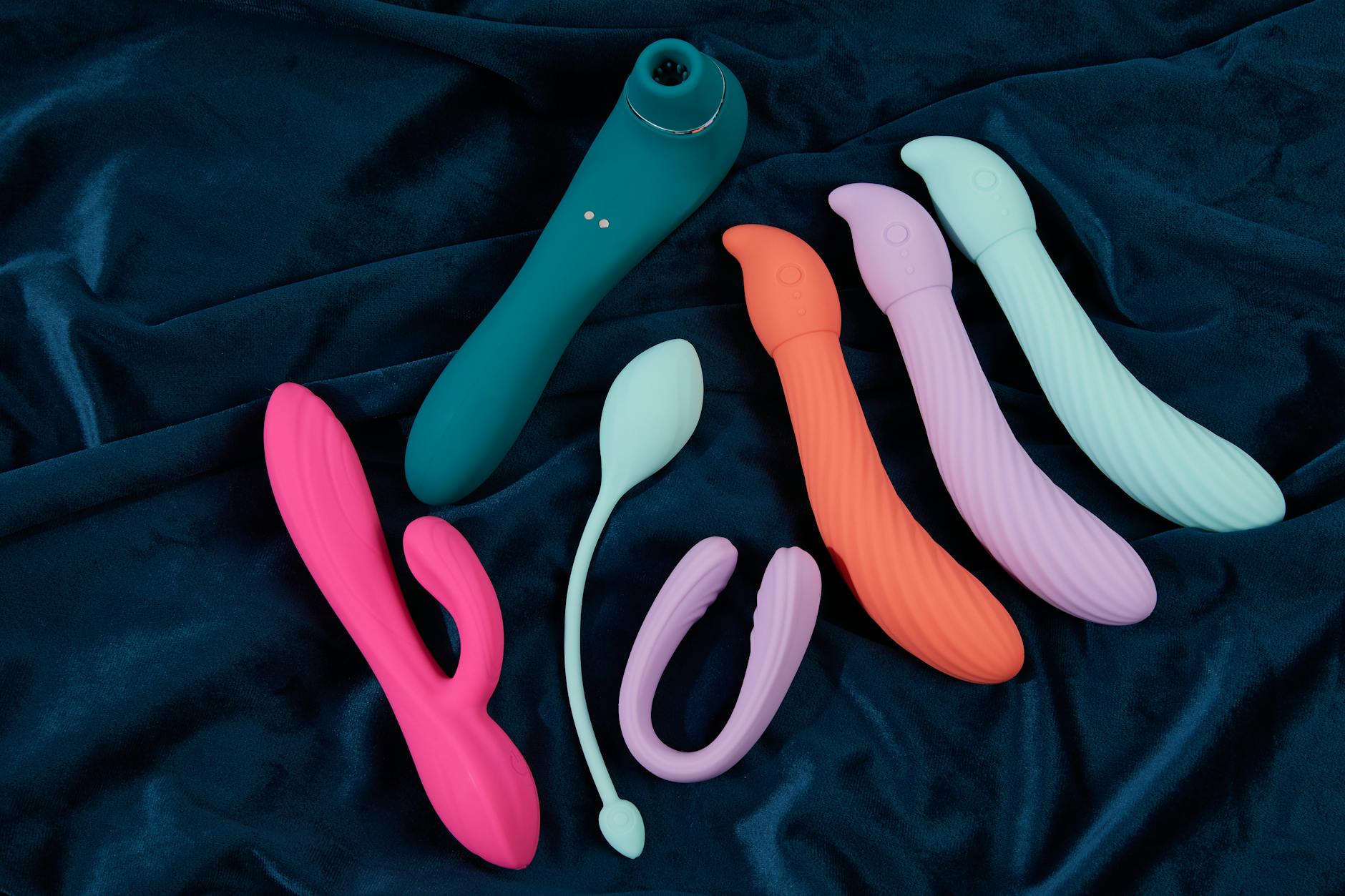 Hand holding a blue silicone clitoral vibrator against a purple background, representing pleasure recovery.