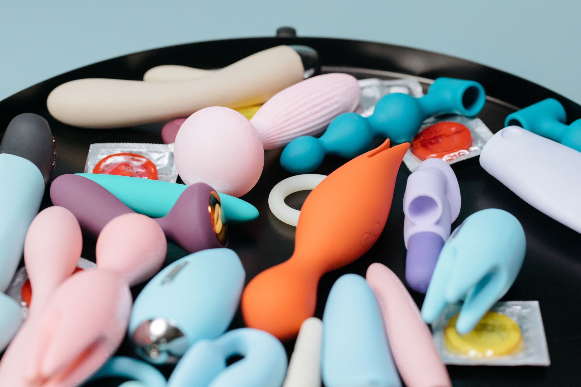 A hand reaching over a variety of colorful sex toys arranged on a table