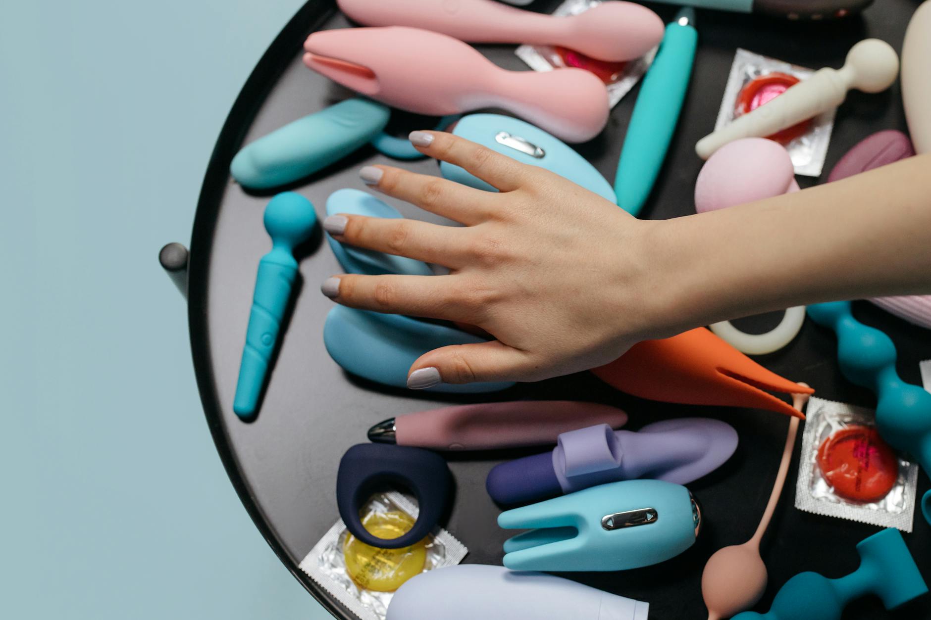 Mulher com óculos segurando vibrador de sucção azul e rosa em postura pensativa