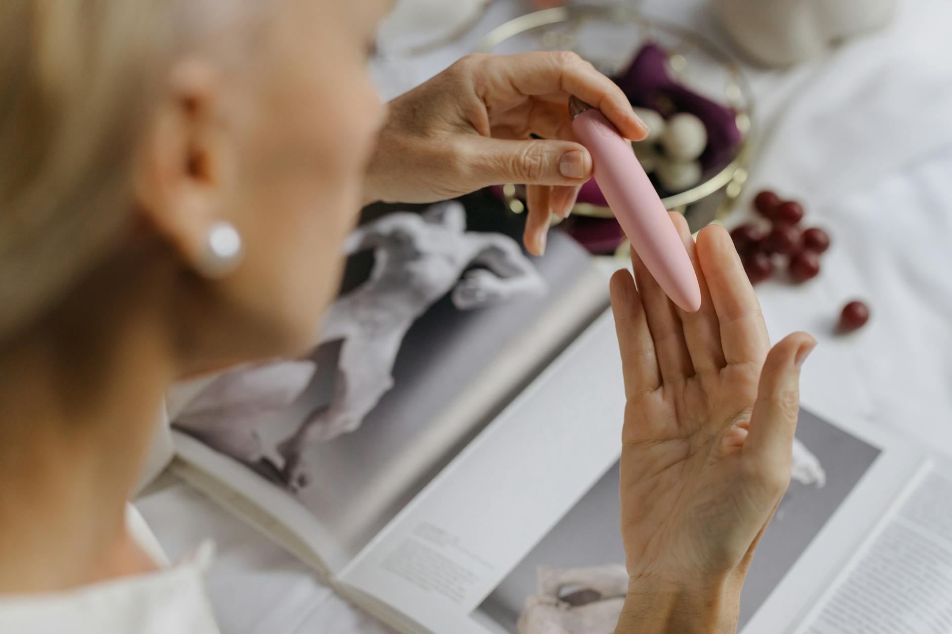 Duas mãos segurando vibradores de silicone rosa e azul contra fundo pastel