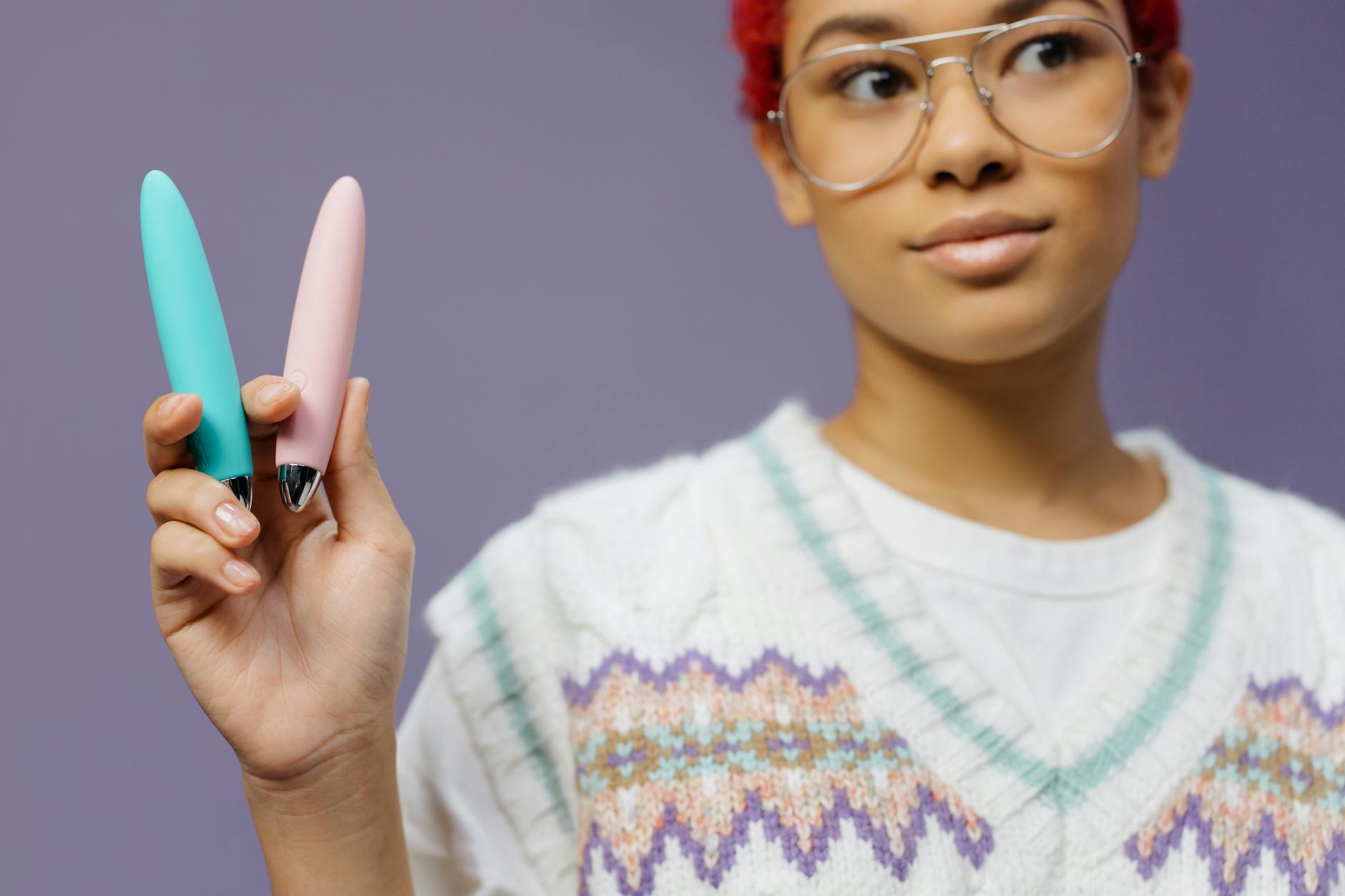 Mulher segurando dois vibradores coloridos contra fundo roxo