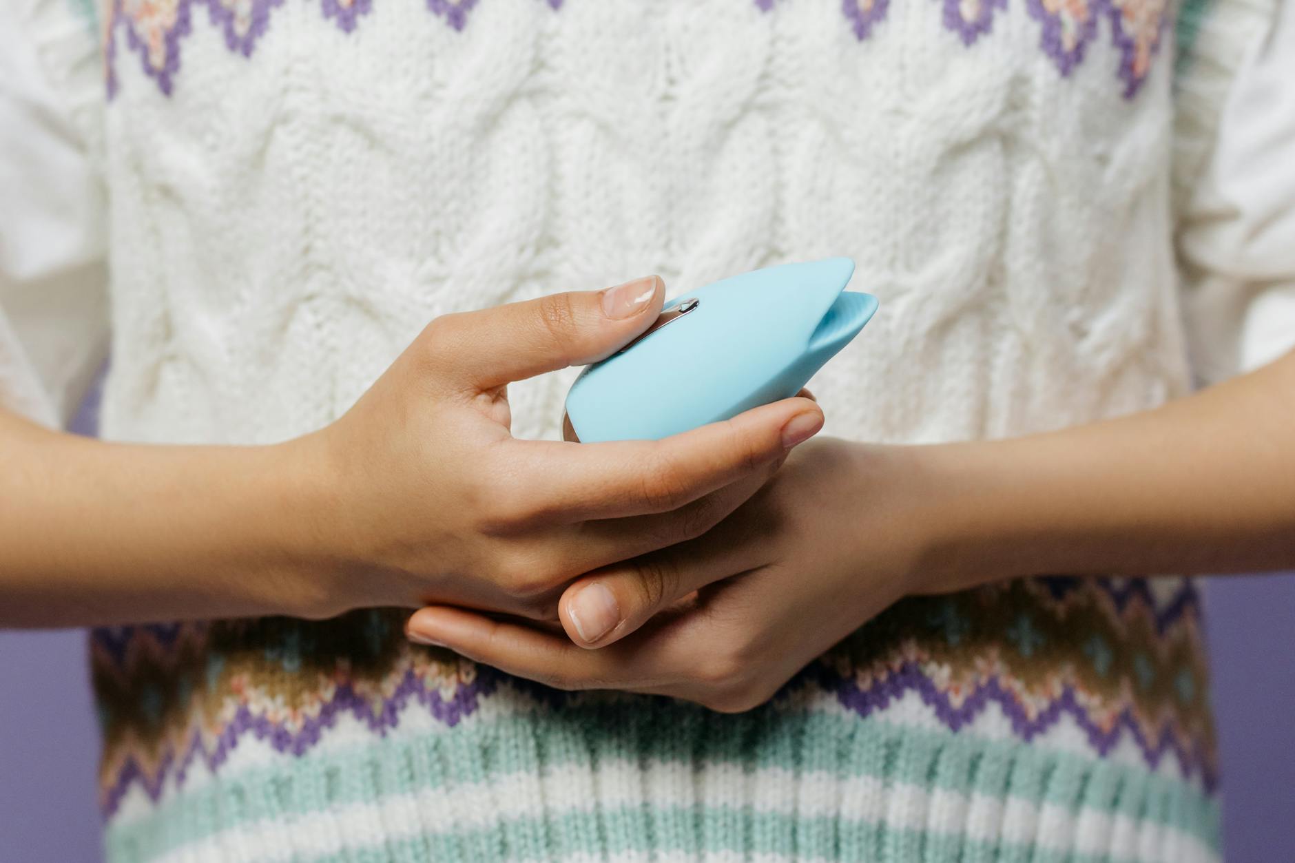 Um vibrador azul em close rodeado por uma mão segurando um suéter de malha