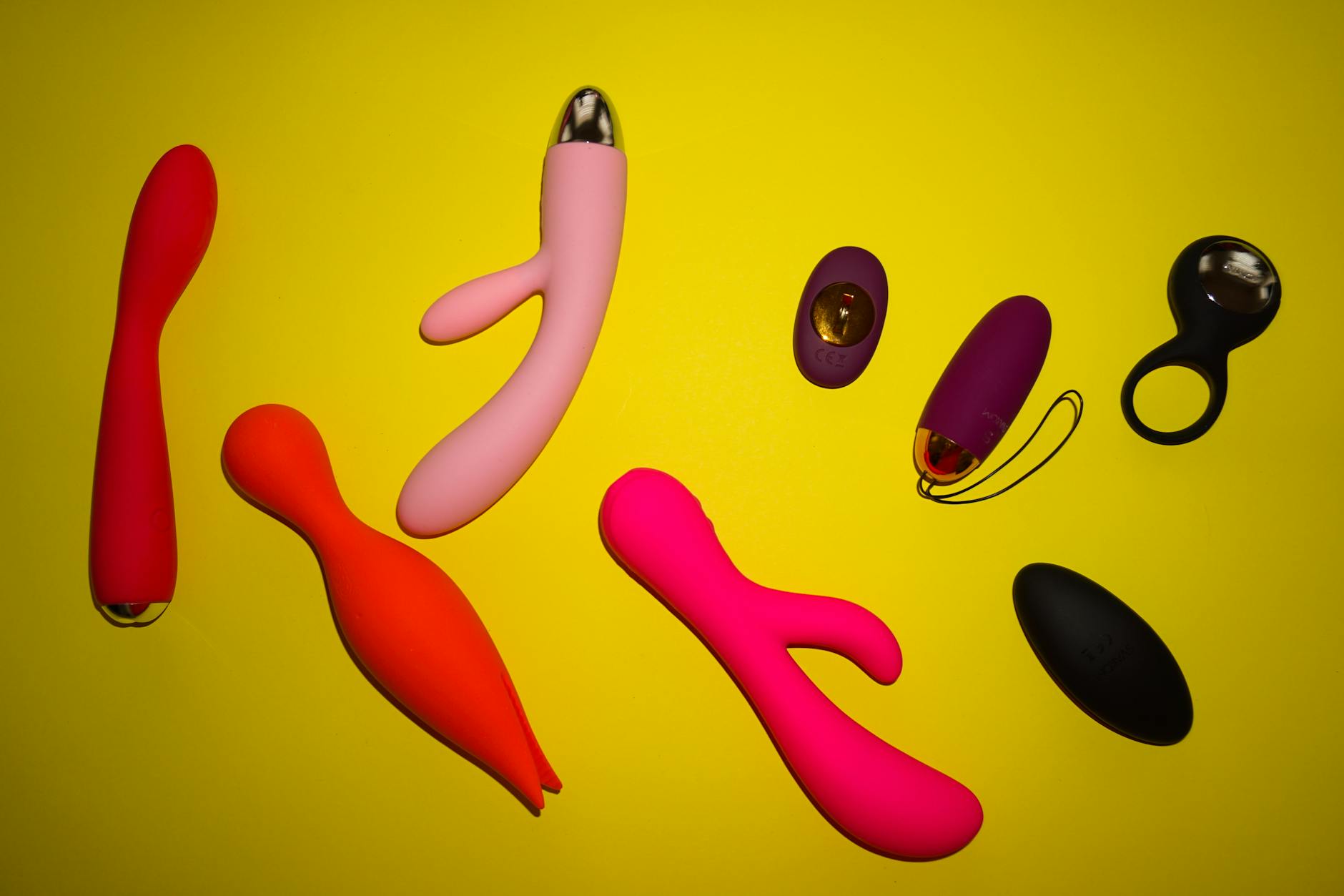 Diversos vibradores coloridos dispostos em superfície amarela brilhante, mostrando design e diversidade
